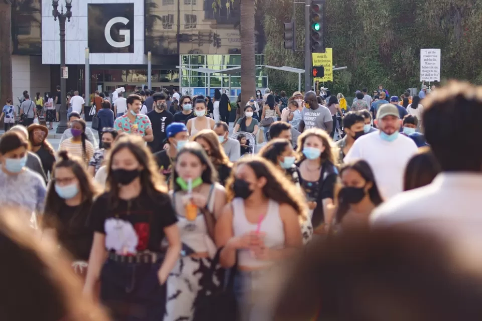 Large numbers of young people, some wearing and masks and others note, walk around an outdoor shopping mall in Southern California.